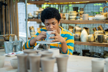 Creative American boy artist molding clay on pottery workshop