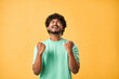 Yes! Emotion of joy, celebration of victory, winning. Handsome Indian man sincerely rejoices with closed eyes and makes winning gesture while standing on yellow background.