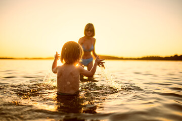 Wall Mural - Cute toddler boy and his teenage sister playing by a lake on hot summer day. Adorable child having fun outdoors during summer vacations.