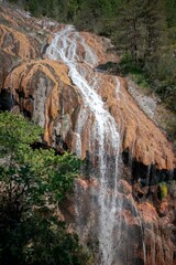 Sticker - Vertical shot of a waterfall surrounded by trees on the mountain on a sunny day