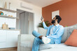 © Prostock-studio - Relaxed Indian Man Turning On Air Conditioner Sitting At Home
