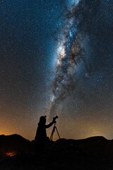 Wall Mural - vertical shot of a person in shadow with a telescope looking at starry sky