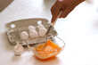 Frau schlägt mit einem Scheebesen rohe Eier zu Rührei