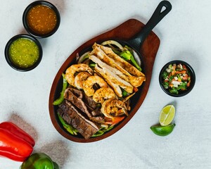 Poster - Top view of mixed meat fajitas in a pan on a wooden board with salsa, pico de gallo, and peppers