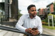 © DusanJelicic - A portrait of a handsome Black businessman leaning against a railing during his break, holding a phone in his hand. With a relaxed posture and a thoughtful expression.