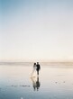 Beautiful vertical back shot of a newly wed couple walking barefoot on the beach