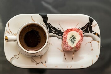 Canvas Print - Top view of a cup of coffee and a dessert on a white plate on a glass table.