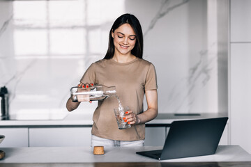 Young woman drinks water at her workplace in kitchen at home