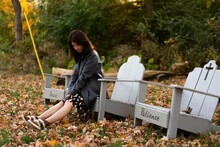 Asian Young Female Sitting On The White Wooden Church Chair In Fallen Autumn Leaves