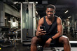 © Богдан Маліцький - young athletic african american man sits in dark gym and uses smartphone, sports guy types online on the phone