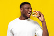 © Богдан Маліцький - african american man in white t-shirt holding big burger and smiling, the guy eats fast food on yellow background