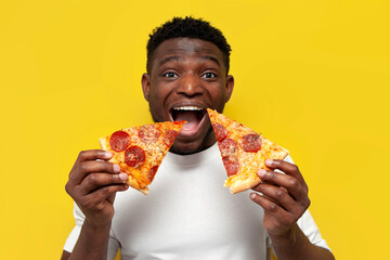 happy african american man in white t-shirt holding two slices of pizza and smiling over yellow background