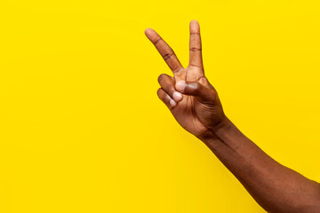 peace gesture on yellow isolated background, african american man's hand shows v-shaped symbol