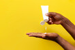 © Богдан Маліцький - hand of african american man holds white tube of cosmetic cream on yellow isolated background