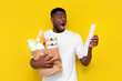 © Богдан Маліцький - shocked african american male shopper holding eco bag with groceries and looking at check and cost