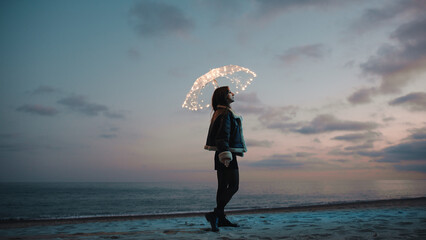 Wall Mural - Glowing umbrella of a girl walking on the beach in the night outdoor