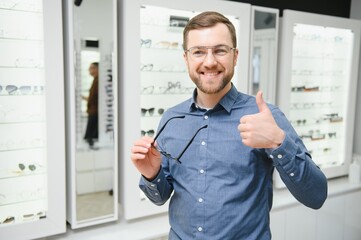 Poster - In Optics Shop. Portrait of male client holding and wearing different spectacles, choosing and trying on new glasses at optical store. Man picking frame for vision correction, closeup.