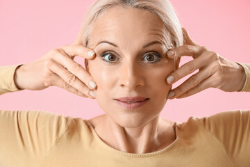 Poster - Mature woman doing face building exercise on pink background, closeup