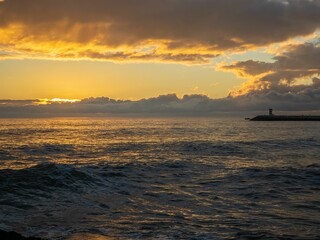 Wall Mural - Beautiful sunset on the seashore with a lighthouse silhouette in the background