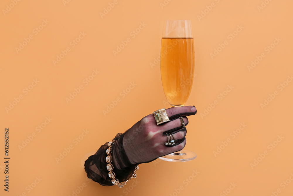 Hand of young woman in gloves wearing stylish jewelry with champagne visible through torn orange paper