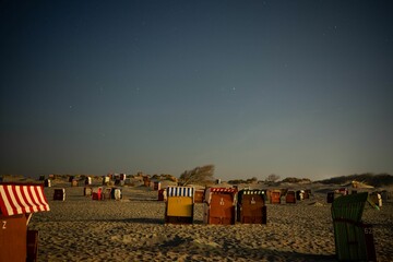 Closed beach chairs on the sand of a coast under the blue starry sky at night