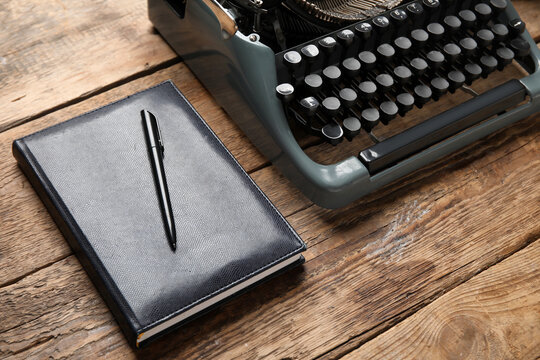 Vintage typewriter with notebook and pen on brown wooden background