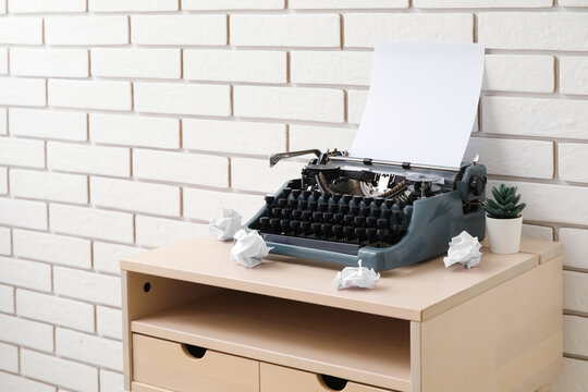 Vintage typewriter with crumpled paper and houseplant on table near brick wall
