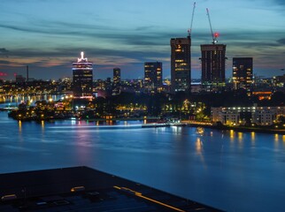 Sticker - View of a river with Adam tower and modern buildings in the background in the evening, Amsterdam