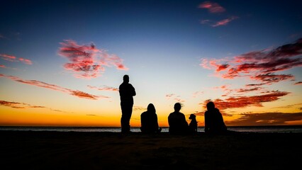 Canvas Print - Silhouette of people watching vibrant sunset from the seashore