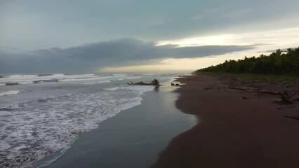 Sticker - Aerial view of the sea waves splashing over the shore at sunset with a cloudy sky in the background