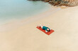 © Marc Tran/Stocksy - woman in swimsuit lie down on red mat for sunbath and relax on beach