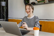 © DZ FILM/Stocksy - A woman laughs while using a laptop indoors