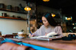 © Ezequiel Giménez/Stocksy - Pensive Asian woman taking notes during studies in cafe