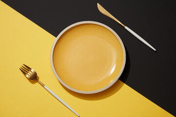 Yellow ceramic plate with knife and fork on yellow and black background. Pop art design. Minimal art background for advertising food product. Top view, table setting