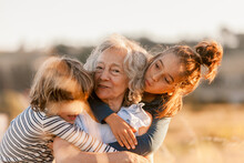Grandmother And Grandchildren Hug Each Other Happily By The Field