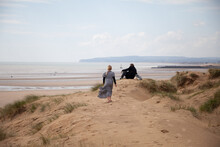 Tween Girl Walks Across A Sand Dune To Her Father.
