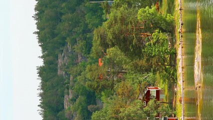 Wall Mural - Vertical Footage Video. Many Red Swedish Wooden Sauna Logs Cabins Houses On Island Coast In Summer Cloudy Day.