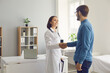 © Studio Romantic - Healthcare and medicine. Friendly smiling middle-aged female doctor shakes hands with young male patient welcoming him in her medical office. Concept of hospital visit and doctor-patient relationship.