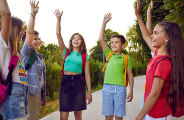 Wall Mural - Group of overjoyed friends having fun in the park. Bunch of cheerful school kids playing games outdoors. Happy, joyful children standing on a park path and raising hands up. Teamwork and fun concept