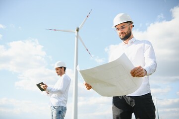 A team of male engineers working together at wind turbine generator farm.