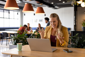 Happy plus size caucasian casual businesswoman making video call using laptop at desk