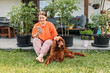 © mdyn - Beautiful Irish Setter dog is laying on grass, while girl using smartphone next to him. Cheerful happy young redhead woman relaxing with her dog in the yard of the house in summer. Full body