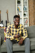 © JustLife - Young man watching tv at home. African sitting on the sofa, enjoy at home.