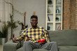 © JustLife - Young man watching tv at home. African sitting on the sofa, enjoy at home.