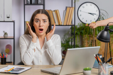 Young business woman working on office laptop with anxiety checking time on clock running late to work being in delay deadline. Manager freelancer girl looking at hour minutes worrying to be punctual