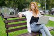 Relaxing young redhead woman sitting in the park and using her laptop.