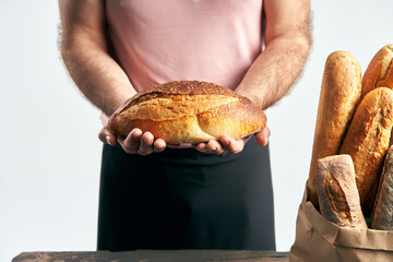 Wall Mural - Baker man in apron holding loaf of fresh baked bread in the hands