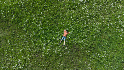 Boy lying on the green grass from above. Top view. Teen in sunasses. Teen looking in camera