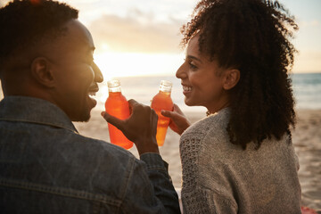 Wall Mural - Smiling young multiethnic couple drinking juice on a beach at sunset