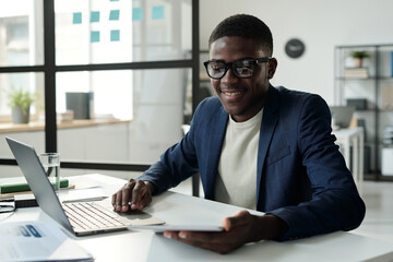 Aufkleber - Young cheerful analyst or broker in eyeglasses and formalwear looking through online financial data on tablet screen while using laptop
